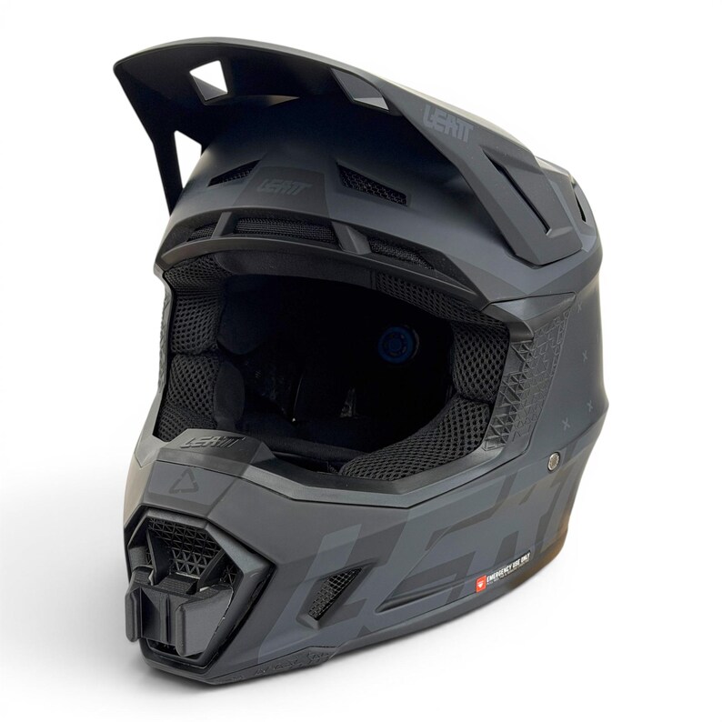 May include: A matte black LEATT motocross helmet with a visor and geometric patterns. The helmet has a chin guard, ventilation, and the brand name is visible. The interior padding is black.