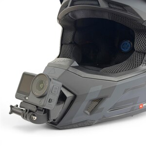 May include: A dark gray motocross helmet with a mounted action camera. The camera is attached to the side of the helmet and has a small screen and a lens. The helmet has a matte finish and a black interior.