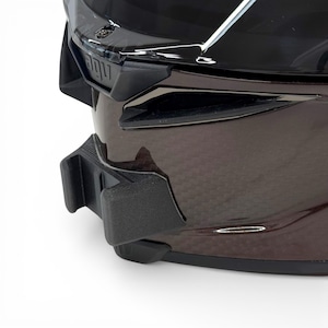 Pu&ograve; includere: Primo piano di un casco da moto con finitura marrone scuro lucida. Il casco presenta componenti aerodinamici neri, tra cui una visiera e attacchi laterali. Il design suggerisce un focus sulla velocit&agrave; e sulla protezione.