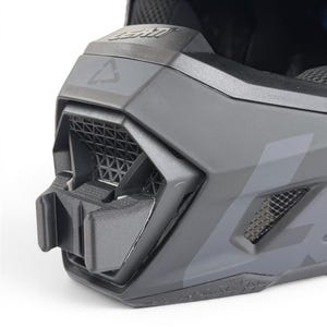 May include: Close-up of a matte gray LEATT brand helmet. The helmet features a geometric design with ventilation grilles and a mounting bracket. The LEATT logo is visible on the top. The helmet is designed for protection and performance.