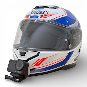 Könnte beinhalten: Weißer, blauer und roter Shoei Motorradhelm mit klarem Visier. Eine Action 5K Kamera ist vorne montiert. Der Helm hat ein stromlinienförmiges Design mit roten und blauen Akzentstreifen. Das Shoei-Logo ist sichtbar.