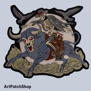 Pode incluir: Etiqueta bordada com um esqueleto montando um touro azul, com dois pássaros pretos voando acima. A etiqueta tem um design detalhado com fundo branco e borda preta.