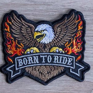 May include: Embroidered patch featuring an eagle with outstretched wings, flames, and the text "BORN TO RIDE" on a banner. The eagle has a white head, brown wings, and yellow talons. The flames are red, orange, and yellow.