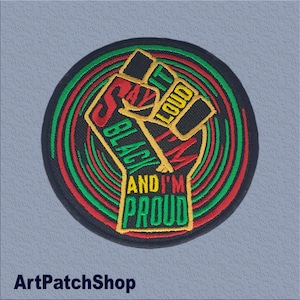 May include: Embroidered patch with a black border and a raised fist design. The fist is outlined in yellow with the words "SAY IT LOUD I'M BLACK AND I'M PROUD" in red, green, and yellow. The background has concentric red and green circles.
