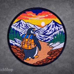 May include: Embroidered patch depicting a penguin with a rucksack walking through a mountain scene. The design includes a sunset, mountains, and trees, with the text "ArtPatchShop" at the bottom.