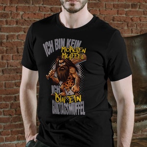 Könnte beinhalten: Schwarzes T-Shirt mit einem Cartoon-Höhlenmenschen, der einen Knüppel hält. Der Text auf dem Shirt lautet "Ich bin kein Morgenmuffel Ich bin ein Ganztagsmuffel".