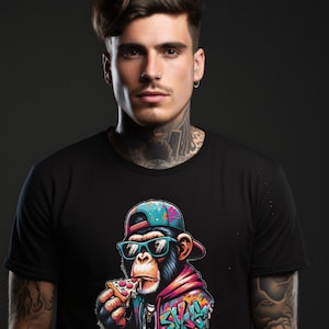 Könnte beinhalten: Schwarzes T-Shirt mit einem Grafikdruck eines Cartoon-Affen, der eine Sonnenbrille und eine Mütze trägt und ein Stück Pizza isst. Der Affe ist von bunten Graffitis umgeben.