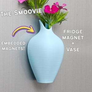 Könnte beinhalten: Eine hellblaue Vase mit eingebauten Magneten, die es ermöglicht, sie an einem Kühlschrank zu befestigen. Die Vase ist mit "The Smoovie" und "Fridge Magnet + Vase" beschriftet.