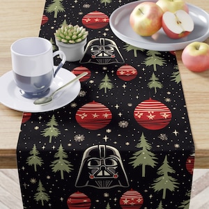 May include: A black table runner with a festive pattern featuring red ornaments, green Christmas trees, and a Darth Vader graphic. The runner is decorated with white stars and snowflakes, creating a holiday theme.
