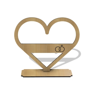 Op de afbeelding: Een houten hartvormige standaard met een platte bovenkant en een basis. De standaard heeft een ontwerp van twee in elkaar grijpende ringen met een diamant bovenop, symbool voor trouwringen.
