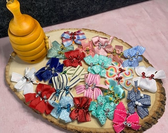 May include: A collection of colorful, decorative bows in various patterns and colors, including red, blue, pink, and striped designs. The bows are arranged on a wooden slice, with a wooden honey pot in the upper left corner.