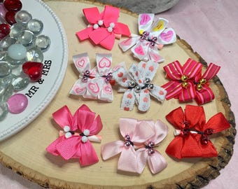May include: A set of ten Valentine's Day themed hair bows. The bows are made of pink, red, and white ribbon and feature hearts, stripes, and polka dots. Some bows have small beads or charms.