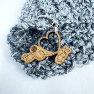 May include: A wooden heart-shaped stitch marker with a silver loop. The marker is attached to a gray crocheted hat.