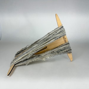 May include: A wooden yarn swift with a gray and white yarn wound around it. The swift is labeled "WoolStitch".