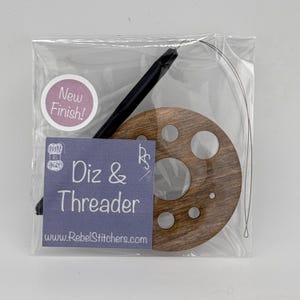 May include: A wooden threader with multiple holes for different sized needles, a black needle threader, and a length of thread. The packaging has a sticker that says "New Finish!" and a label that says "Diz & Threader www.RebelStitchers.com"
