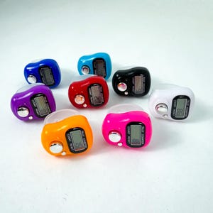 Puede incluir: Ocho contadores de dedos en diferentes colores, incluyendo morado, naranja, rosa, blanco, negro, azul, rojo y azul claro. Cada contador tiene una pantalla digital con las palabras "Tally Counter", "Count" y "Reset".