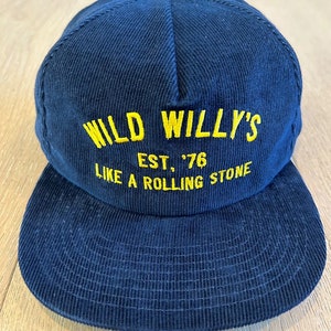 Puede incluir: Una gorra de béisbol de pana azul marino con texto bordado en amarillo que dice "WILD WILLY'S EST. '76 LIKE A ROLLING STONE"