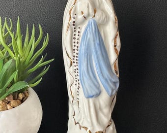 Puede incluir: Estatua de cerámica blanca de la Virgen María, con velo azul y detalles dorados. La estatua tiene una expresión serena y junta las manos en oración. Un rosario cuelga de su cuello. La base tiene ribetes dorados.