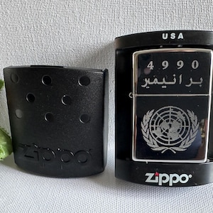 May include: A black Zippo lighter with the United Nations emblem and Arabic text. The lighter is in its original black case, and the packaging reads "USA". The lighter is in a black case with the Zippo logo.