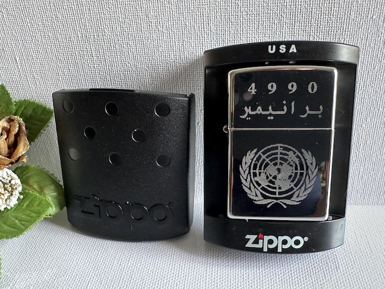 May include: A black Zippo lighter with the United Nations emblem and Arabic text. The lighter is in its original black case, and the packaging reads "USA". The lighter is in a black case with the Zippo logo.
