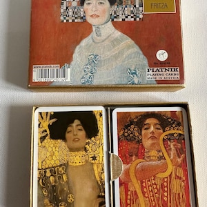May include: A deck of playing cards featuring artwork by Gustav Klimt. The box displays a portrait of a woman with the text "GUSTAV KLIMT FRITZA" and "PIATNIK PLAYING CARDS MADE IN AUSTRIA". The cards inside showcase Klimt's iconic art style.