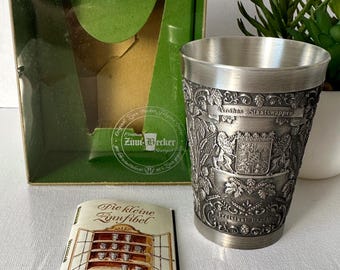 Puede incluir: Un tanque de peltre plateado con un diseño en relieve de un escudo de armas y el texto "Grosses Staatswappen" y "Freistaat Bayern". El tanque está en una caja con un interior verde y un folleto titulado "Die kleine Zinnfibel" con el texto "Mit Pflegetips".