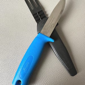 Peut inclure: Un couteau à lame fixe avec un manche texturé bleu vif et une lame en acier argenté. Le manche porte le texte en relief "Frosts". Le couteau est accompagné d'un étui en plastique noir doté d'une attache pour ceinture.