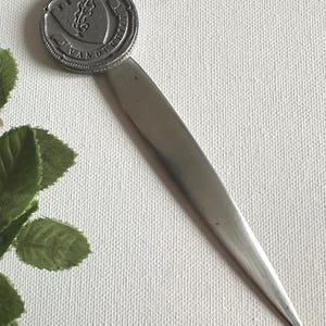 May include: A silver letter opener with a circular emblem at the top. The emblem features a shield design with the word "VANDERBILT" around the edge. The opener has a long, slender blade.