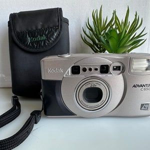 May include: A silver Kodak Advantix C650 film camera with a black lens and a black carrying case. The camera has a zoom lens with a 2x zoom.