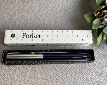 Puede incluir: Un bolígrafo Parker plateado con un cartucho de tinta azul en una caja blanca con un patrón blanco y negro y la palabra "Parker" impresa en él.