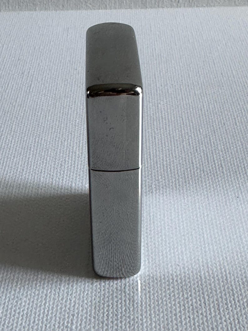 May include: A silver-colored, rectangular lighter with a hinged lid. The lighter has a smooth, reflective surface and a classic design. The lighter is shown against a white background.