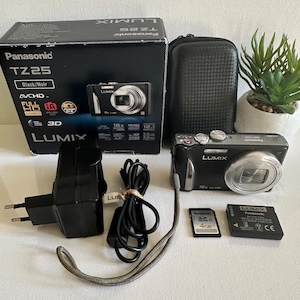 Può includere: Una fotocamera digitale Panasonic Lumix TZ25 nera con accessori, tra cui un caricabatterie, una custodia e schede di memoria. La fotocamera è argento e nera, con il logo Lumix visibile. La scatola dice "TZ25 Black/Noir".