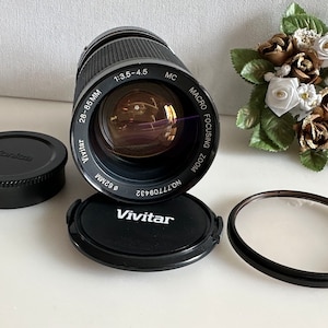 May include: A black Vivitar 28-85mm 1:3.5-4.5 MC Macro Focusing Zoom lens with a black lens cap, a black filter, and a black lens hood.