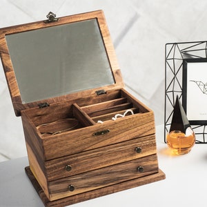 Elegant wooden jewelry box with a rich grain pattern, featuring three drawers with brass handles, and a hinged top lid with an interior mirror