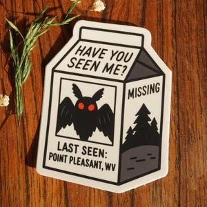 May include: A white sticker in the shape of a milk carton with the text "HAVE YOU SEEN ME?" and "MISSING". It features a black moth with red eyes and the text "LAST SEEN: POINT PLEASANT, WV".
