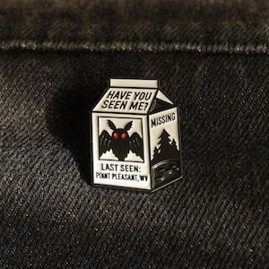 May include: A white and black enamel pin in the shape of a milk carton. The pin features a moth with red eyes and the text "HAVE YOU SEEN ME?" and "MISSING". The text "LAST SEEN: POINT PLEASANT, WV" is also included.