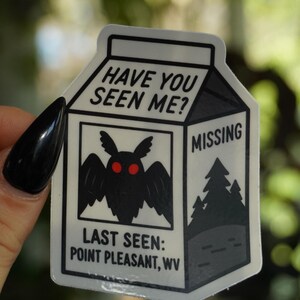 May include: A white sticker in the shape of a milk carton with the text "HAVE YOU SEEN ME?" at the top. The sticker features a black moth with red eyes and the word "MISSING". The text "LAST SEEN: POINT PLEASANT, WV" is also included.