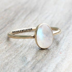 May include: A gold ring with a white oval moonstone. The ring is engraved with the text "DREAMJEWELRYHUB".