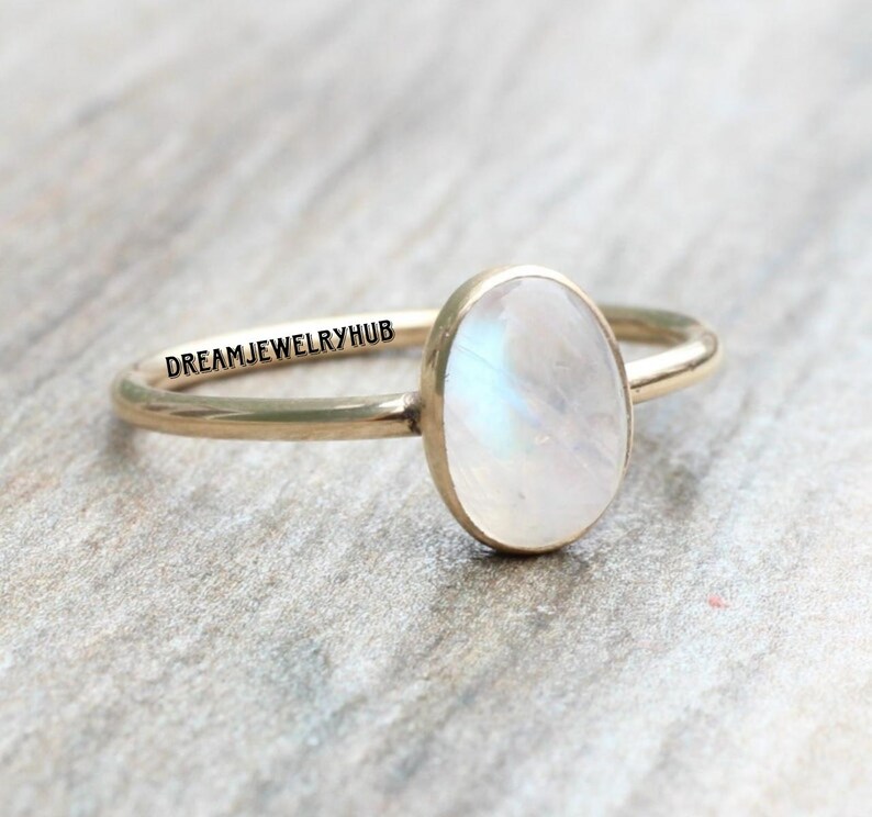 May include: A gold ring with a white oval moonstone. The ring is engraved with the text "DREAMJEWELRYHUB".