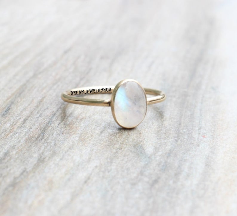 May include: A gold ring with a white oval moonstone. The ring is simple and elegant.