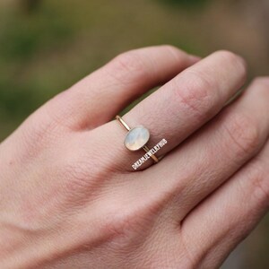 May include: A delicate gold ring with a white oval gemstone. The ring is simple and elegant, perfect for everyday wear.
