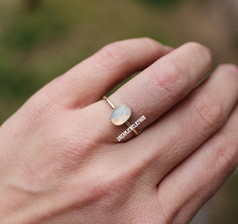 May include: A delicate gold ring with a white oval gemstone. The ring is simple and elegant, perfect for everyday wear.