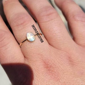 May include: A gold ring with a white oval gemstone. The gemstone has a rainbow iridescent sheen.