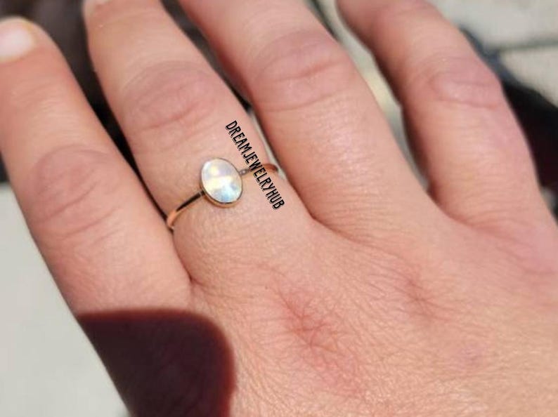 May include: A gold ring with a white oval gemstone. The gemstone has a rainbow iridescent sheen.