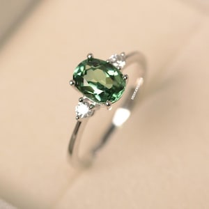 Può includere: Un anello d'argento con una pietra ovale verde e due pietre bianche più piccole sulla fascia.