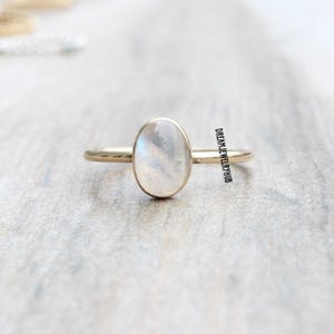 May include: A gold ring with a white oval moonstone. The ring is simple and elegant.
