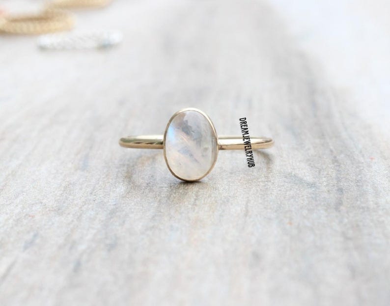 May include: A gold ring with a white oval moonstone. The ring is simple and elegant.