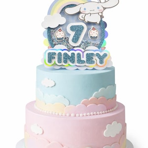 Puede incluir: Una tarta de cumpleaños de dos pisos con glaseado azul pastel y rosa. La tarta está decorada con adornos en forma de nube y un adorno con un personaje de dibujos animados, un arcoíris y el nombre "FINLEY" con el número "7".
