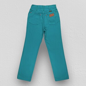 May include: A pair of teal blue denim jeans with a brown leather patch on the back pocket.