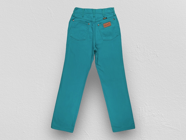 May include: A pair of teal blue denim jeans with a brown leather patch on the back pocket.